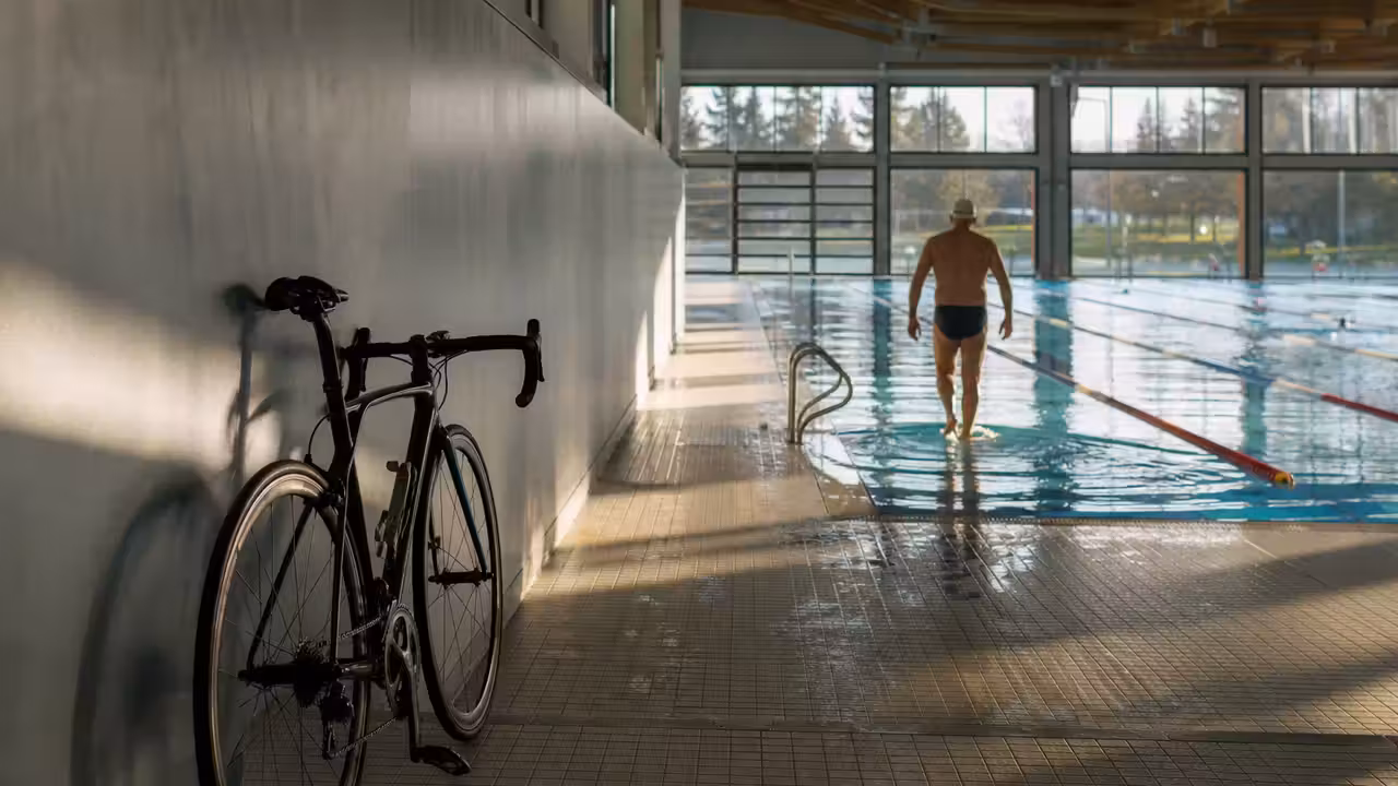 Un vélo posé près d’un bassin intérieur, illustrant l’alternance entre cyclisme et séances de natation.