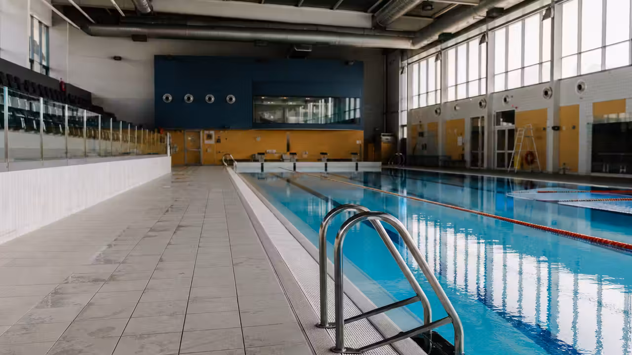 Bassin intérieur d’une piscine municipale vide, avec lignes d’eau et technicien contrôlant la qualité de l’eau