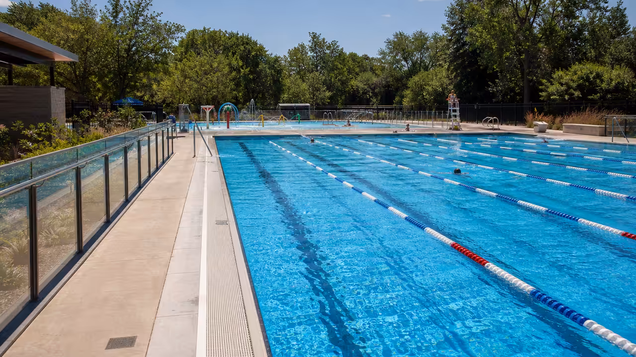 Bassin extérieur rénové d’une piscine municipale, lignes d’eau calmes et plages minérales sous le soleil