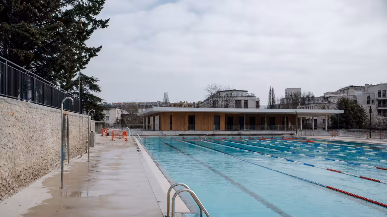 Bassin extérieur d'une piscine municipale rénovée, entouré de vestiaires et d'équipements techniques