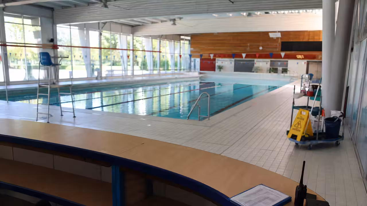 Hall d’une piscine municipale vide avec bassin en arrière-plan et matériel d’entretien rangé