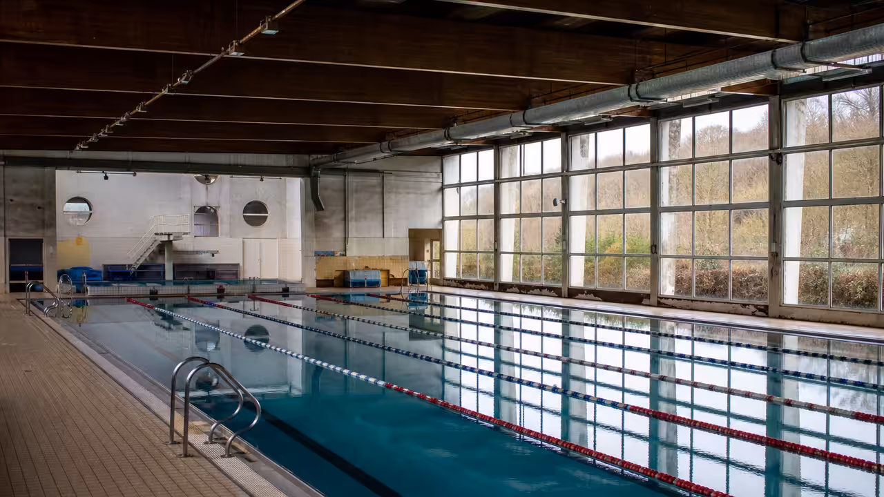 Bassin couvert d’une piscine municipale ancienne, avec lignes d’eau et grandes baies vitrées en lumière naturelle