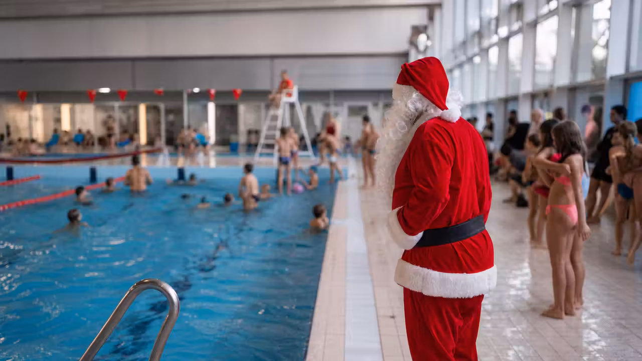 Animateur déguisé en Père Noël au bord d’un bassin couvert, devant des familles réunies pour une animation.