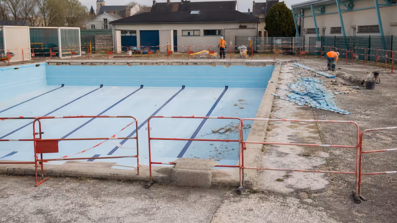 Piscine municipale de plein air en rénovation, avec bassin vide et bâtiment technique en arrière-plan