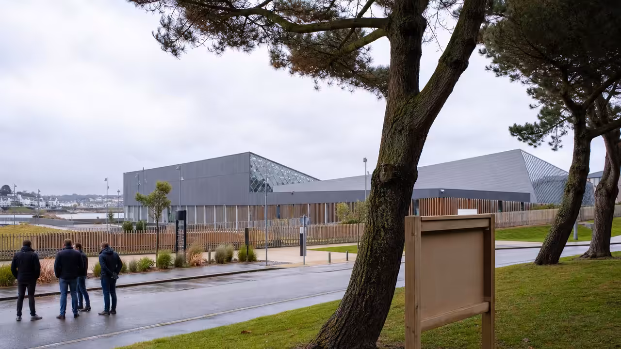 Vue extérieure d’un centre aquatique contemporain près du littoral, avec bassin et aménagements paysagers