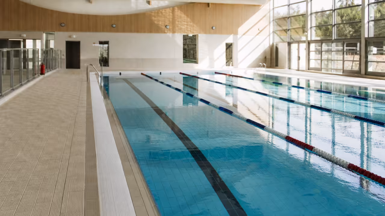 Bassin couvert rénové d’une cité scolaire, lignes d’eau calmes et lumière naturelle entrant par les baies vitrées