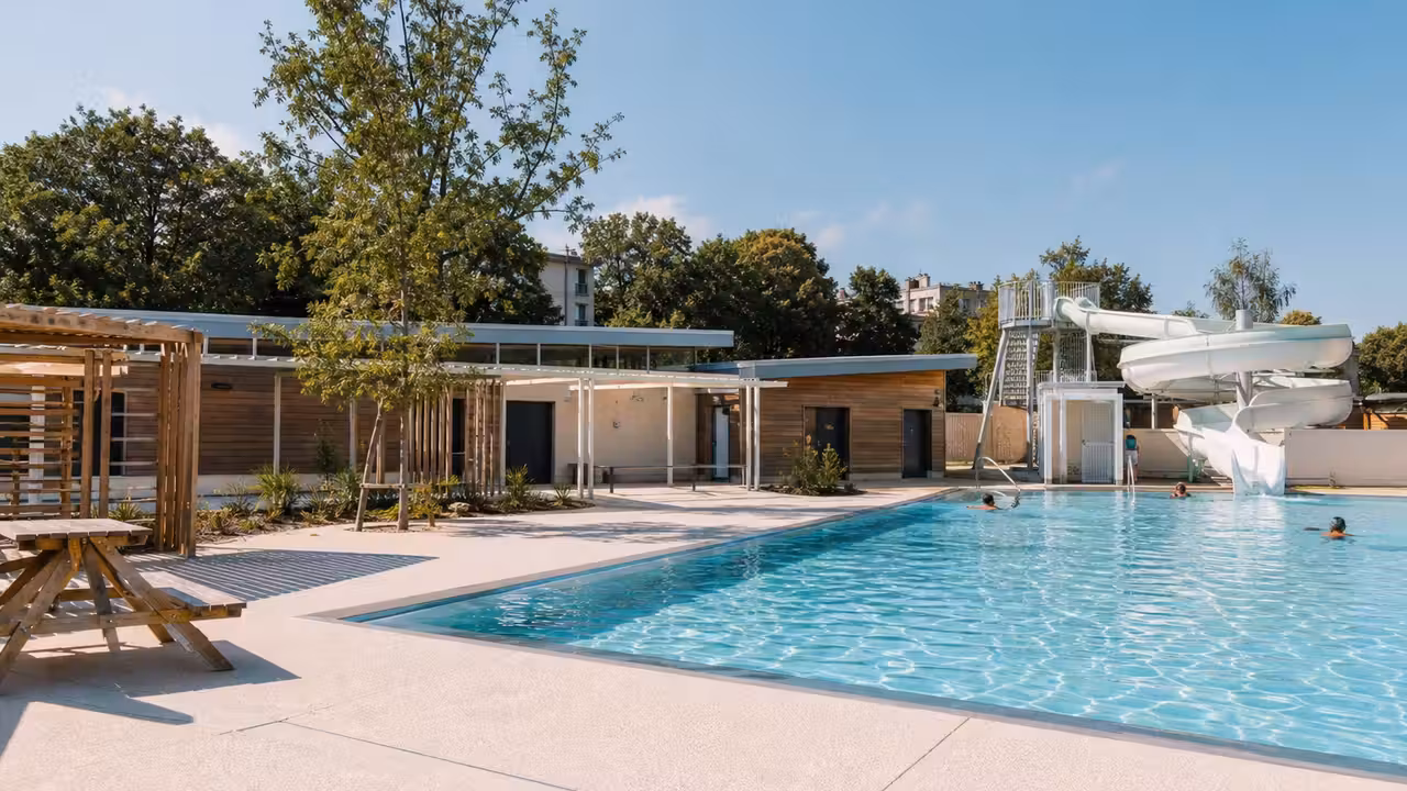 Bassin extérieur de piscine municipale avec toboggan, plage minérale et espaces de détente à Lyon