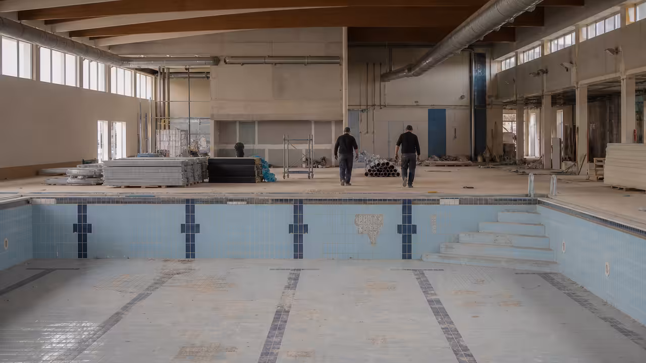 Ancienne piscine municipale en rénovation, avec bassin vide et ouvriers préparant sa reconversion