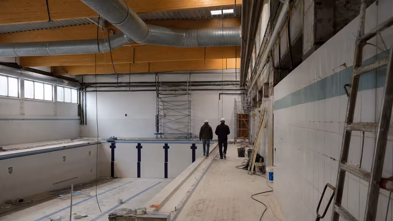 Bassin intérieur lumineux d’une piscine municipale en rénovation, avec baies vitrées et chantier au second plan