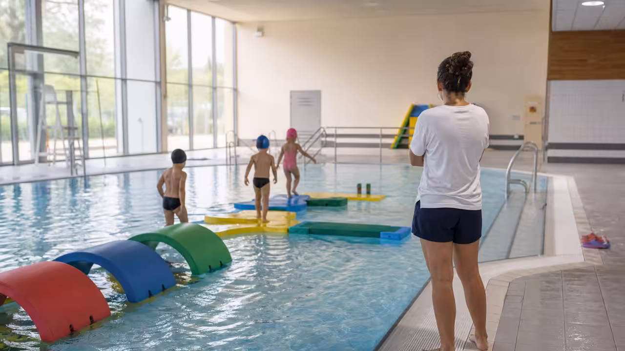 Enfants de maternelle évoluant dans un parcours aquatique ludique sous la surveillance d’un maître-nageur
