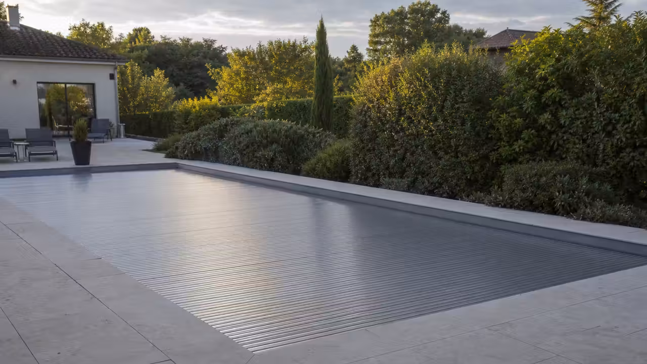 Volet automatique fermé sur une piscine rectangulaire, avec terrasse en pierre et jardin arboré