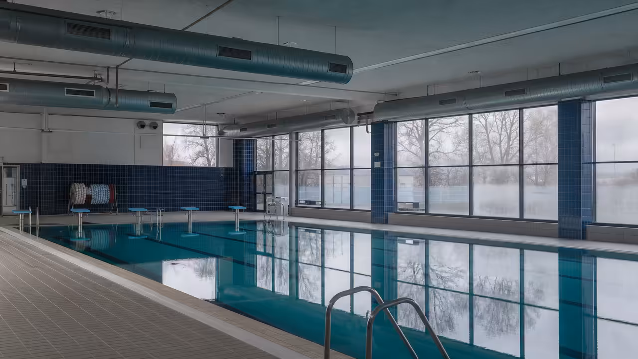 Hall de piscine couverte vide, baies vitrées embuées et bouches de ventilation au-dessus du bassin