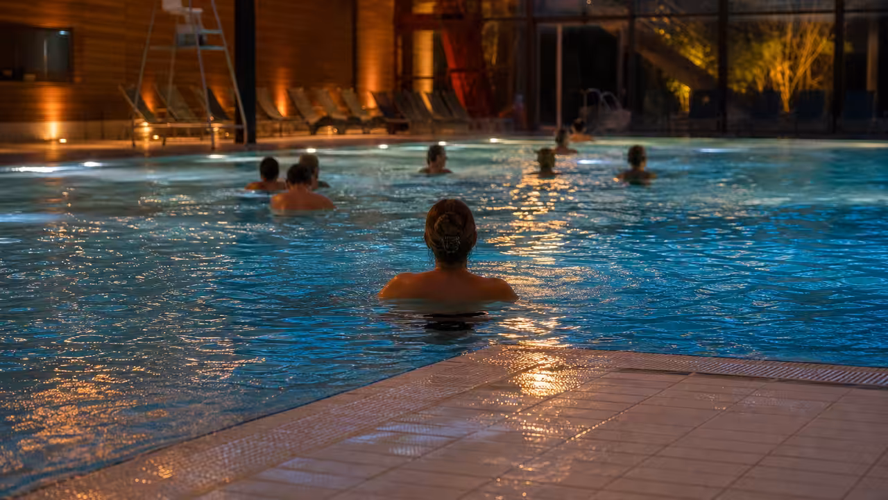 Bassin couvert éclairé en douceur lors d’une soirée bien-être avec des adultes se relaxant dans l’eau
