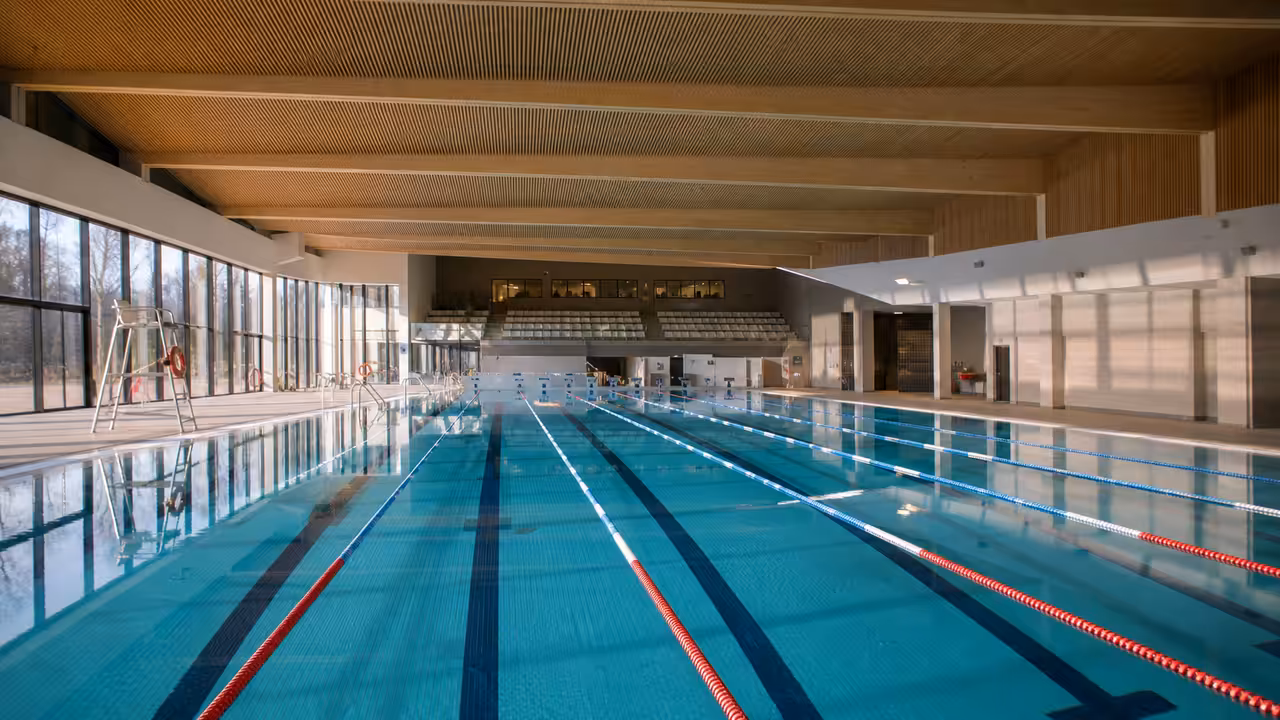 Bassin sportif couvert de 50 mètres avec lignes d’eau, gradins sobres et lumière naturelle latérale