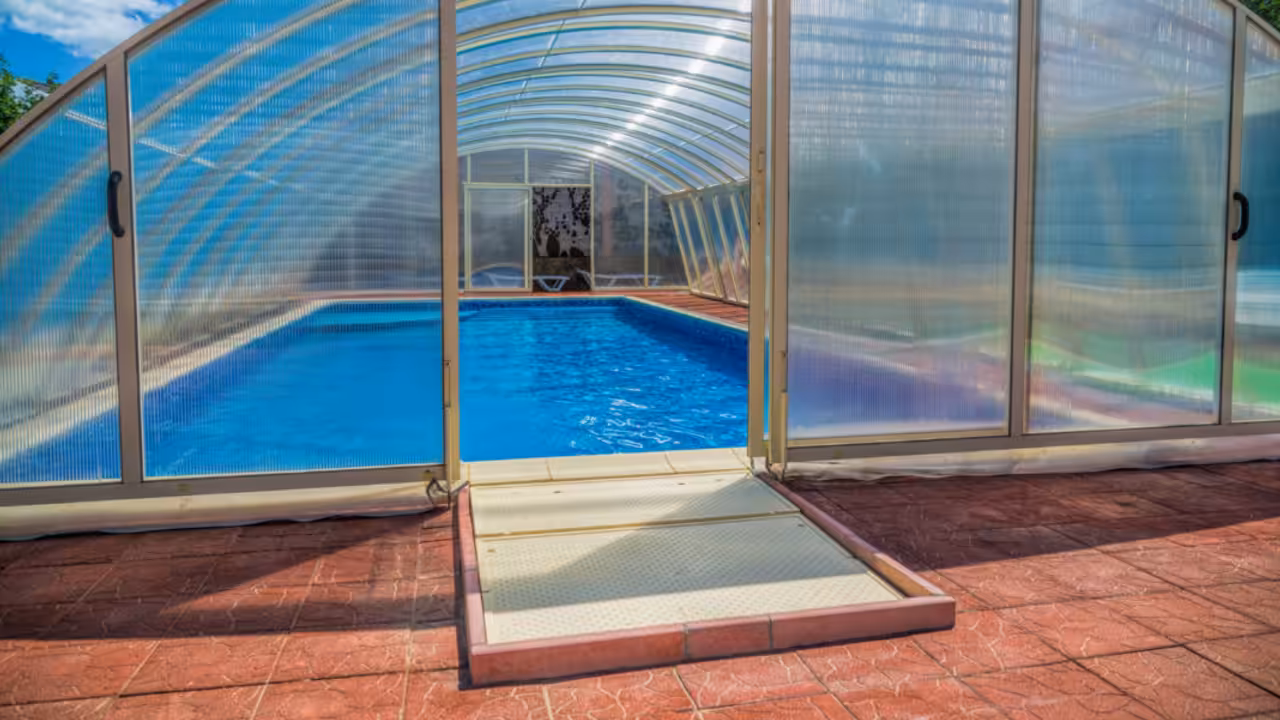 Abri rigide télescopique en aluminium et polycarbonate installé au-dessus d’une piscine enterrée contemporaine