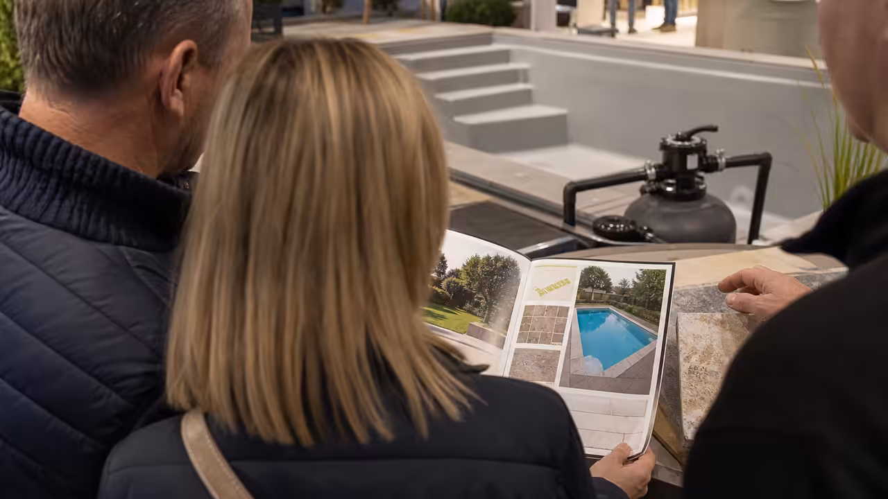 Couple consultant des plans et des échantillons de margelles sur un stand de piscine dans un salon de l’habitat