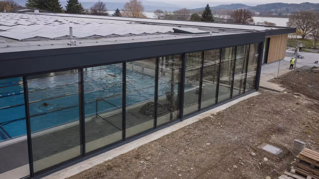 Toiture d’un centre aquatique public équipée de panneaux solaires, avec bassin couvert visible en arrière-plan