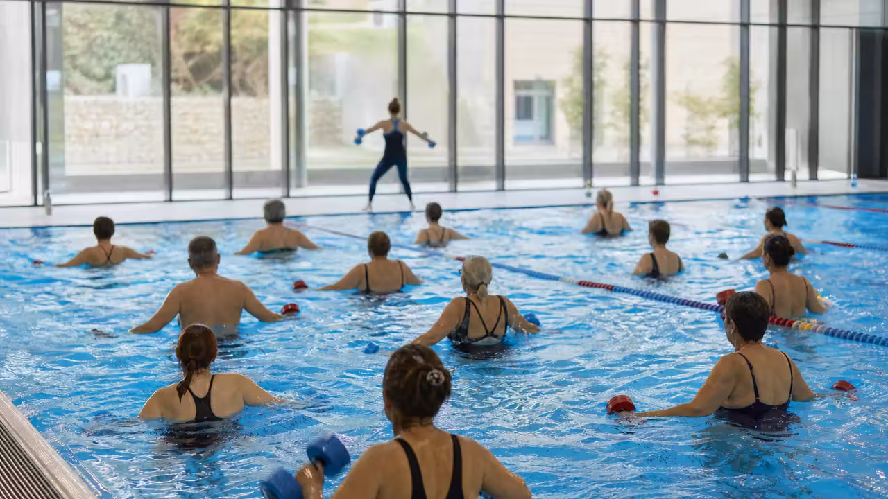 Adultes participant à un cours d’aquagym encadré dans le bassin lumineux d’une piscine publique