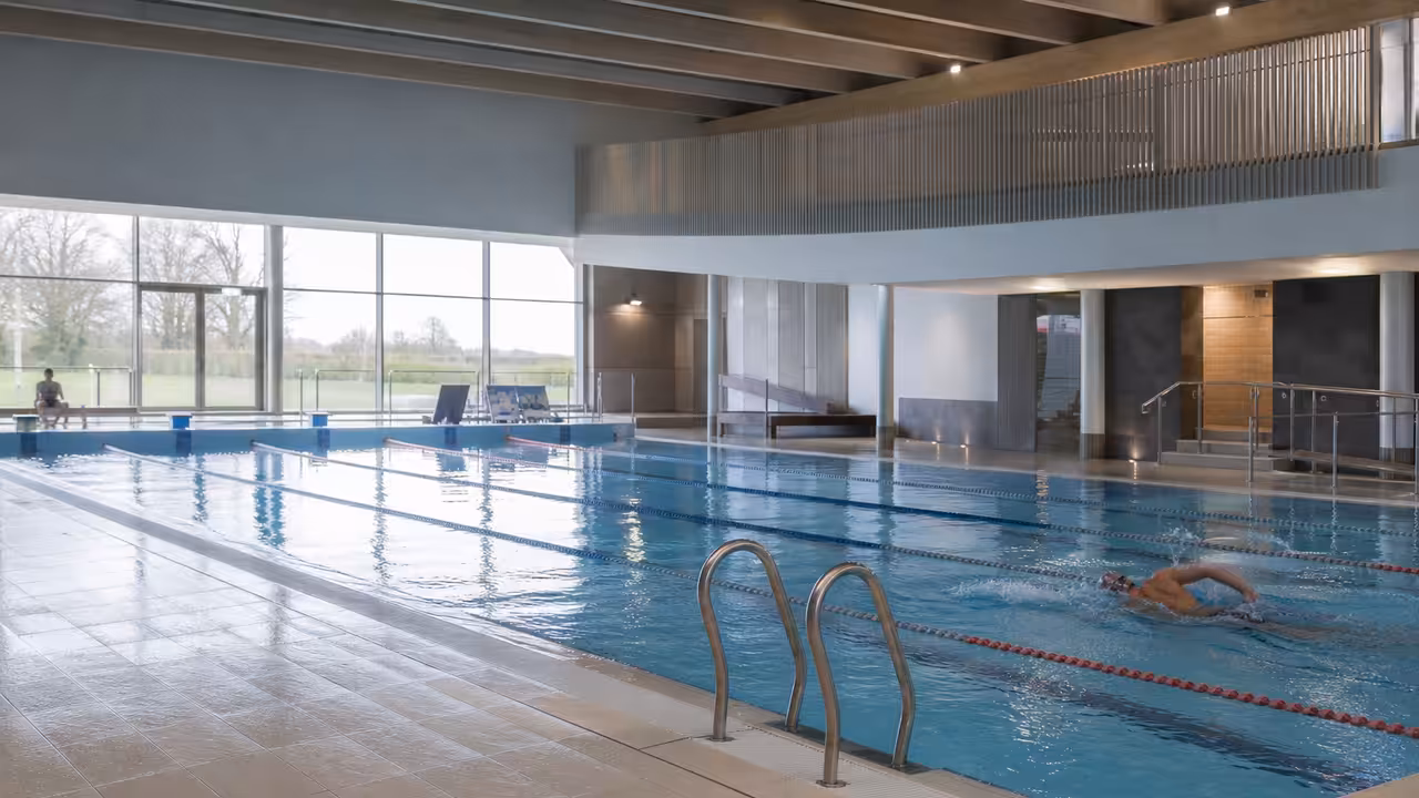 Bassin intérieur de 25 mètres rénové avec lignes d’eau, baies vitrées et plages carrelées lumineuses