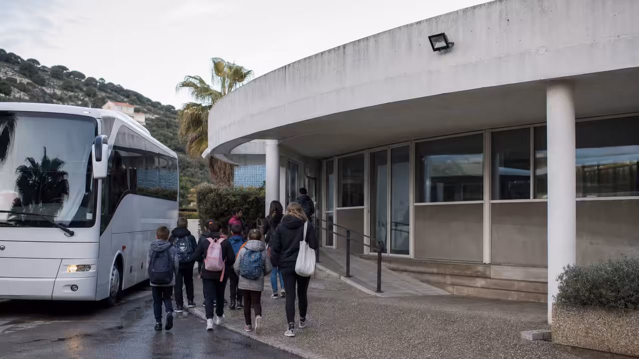 Groupe d’élèves accompagné vers un autocar stationné devant un centre aquatique municipal en milieu urbain