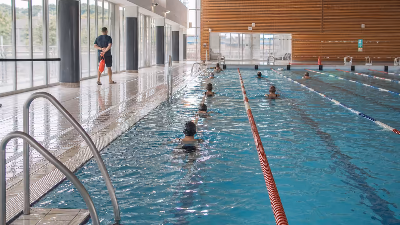 Lignes d’eau d’une piscine municipale où des nageurs s’entraînent sous la surveillance d’un maître-nageur