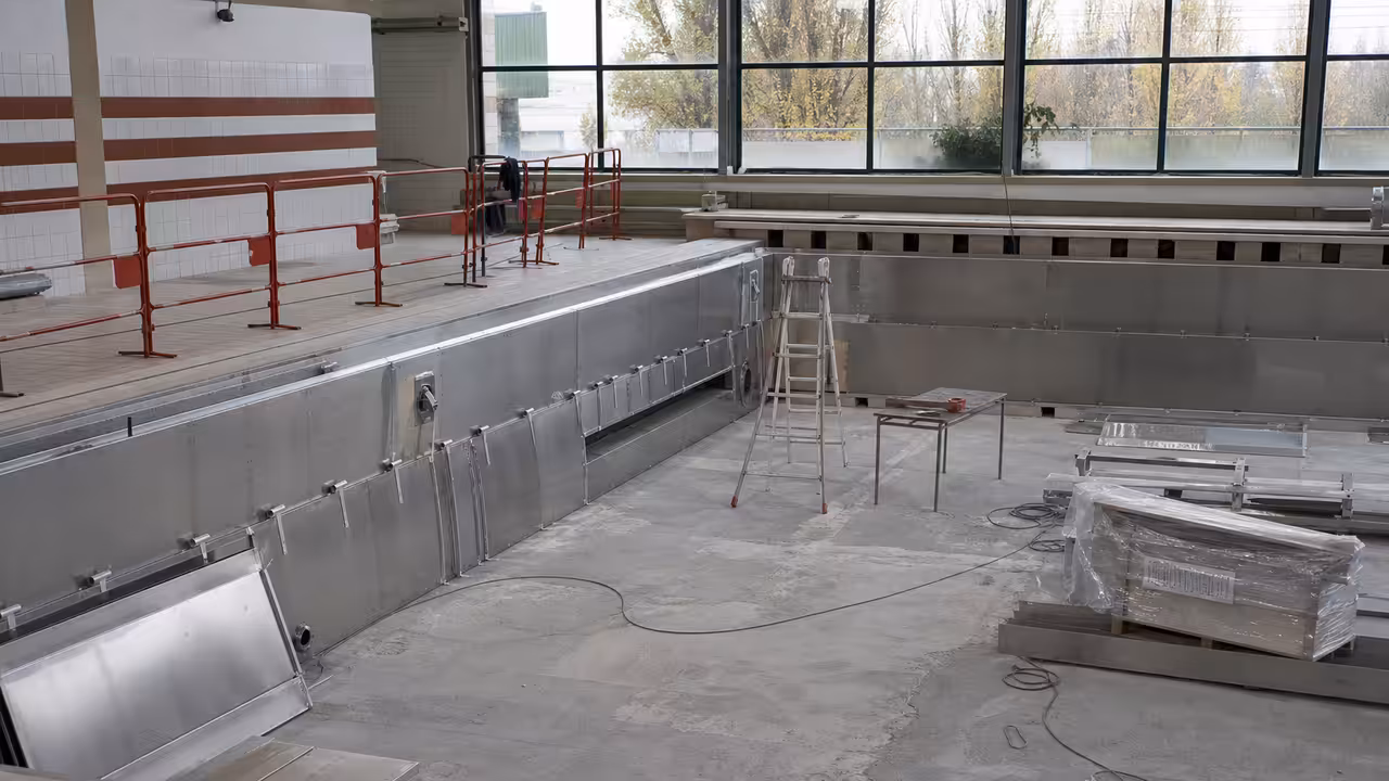 Bassin de piscine publique vide en rénovation, avec revêtement métallique et chantier technique au premier plan