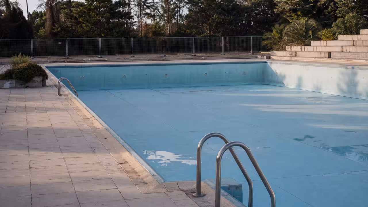 Ancien bassin municipal vide à Anglet, avec plages carrelées et clôture de chantier en arrière-plan