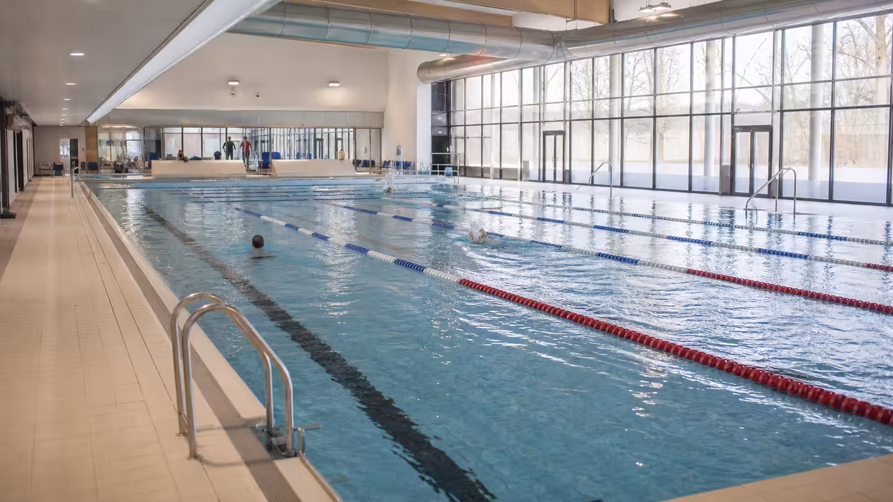 Intérieur lumineux d’une piscine publique rénovée avec lignes de nage, plages carrelées et larges baies vitrées