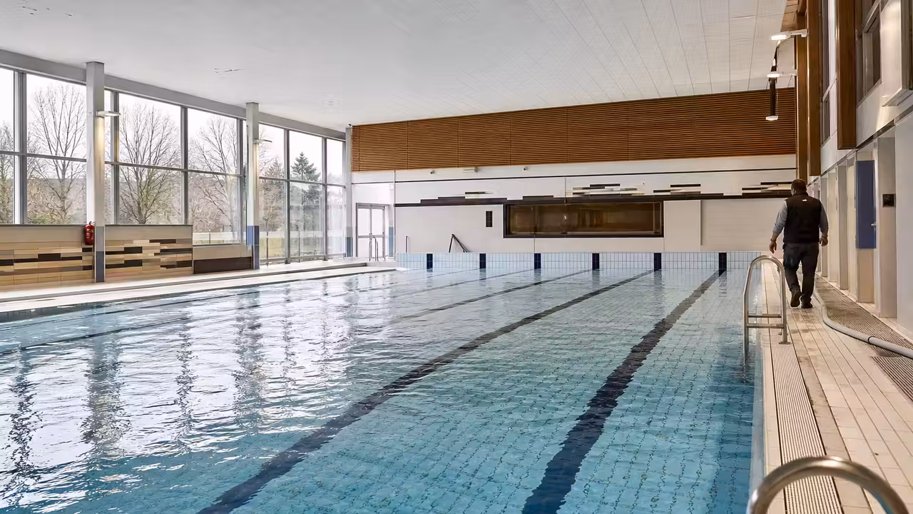 Bassin intérieur d’une piscine municipale rénovée en cours de remplissage, avec lignes d’eau et baie vitrée
