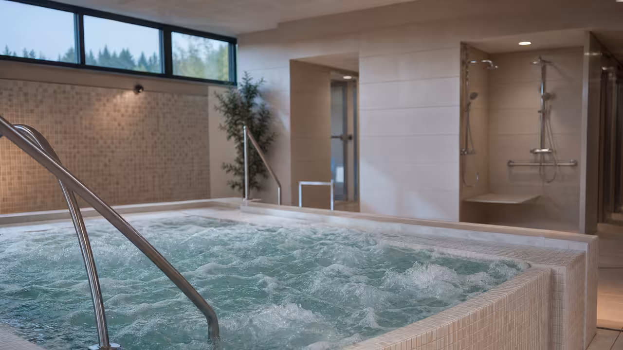 Jacuzzi intérieur rénové d’un centre aquatique, avec carrelage clair, douches modernes et eau en mouvement