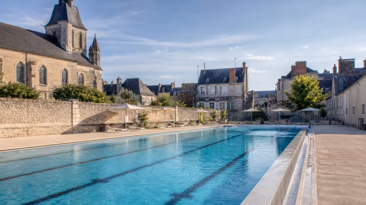 Vue d’ensemble d’une piscine municipale rénovée avec bassin à débordement et espace de repos extérieur