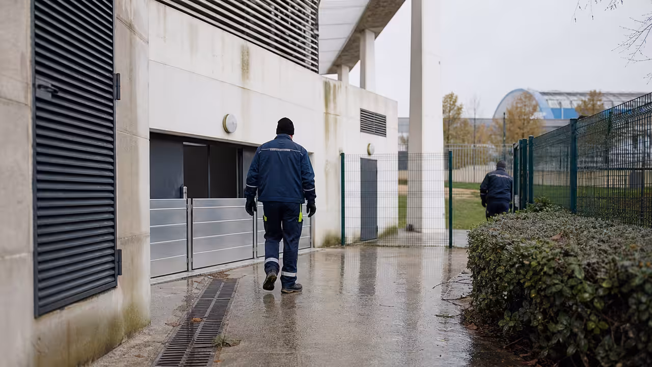 Vue extérieure d’une piscine municipale près d’un cours d’eau après une crue, avec protections temporaires