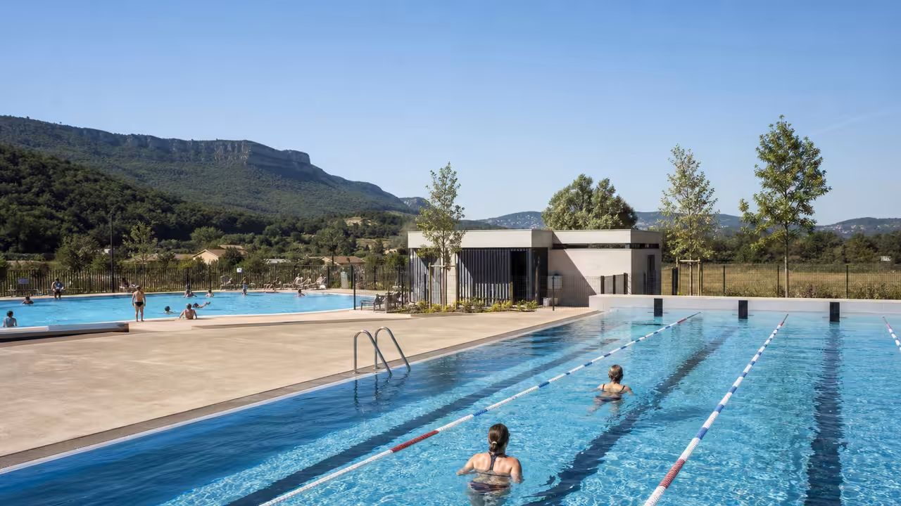 Bassins extérieurs rénovés d’une piscine municipale, avec lignes d’eau, plages claires et local technique en arrière-plan