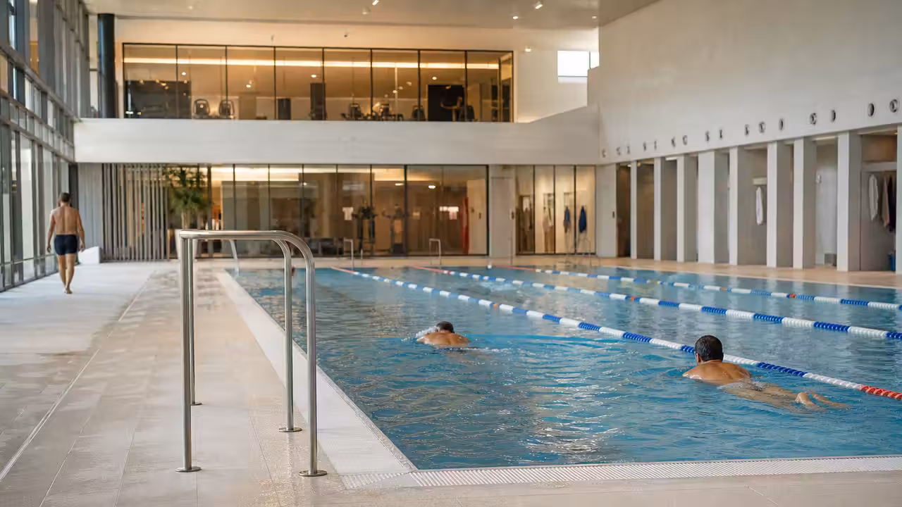 Bassin municipal rénové avec lignes d'eau, plages claires, vestiaires vitrés et baigneurs vus de dos à Avignon