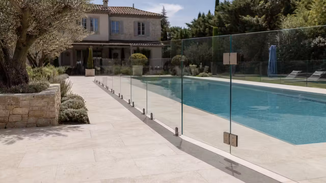 Barrière transparente en verre sécurisant une piscine moderne sur une terrasse en pierre claire
