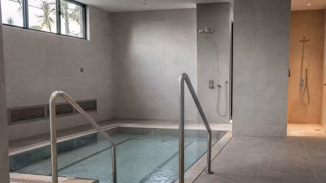 Espace d’hydrothérapie sportif contemporain avec bassin de récupération, douche et matériaux minéraux clairs