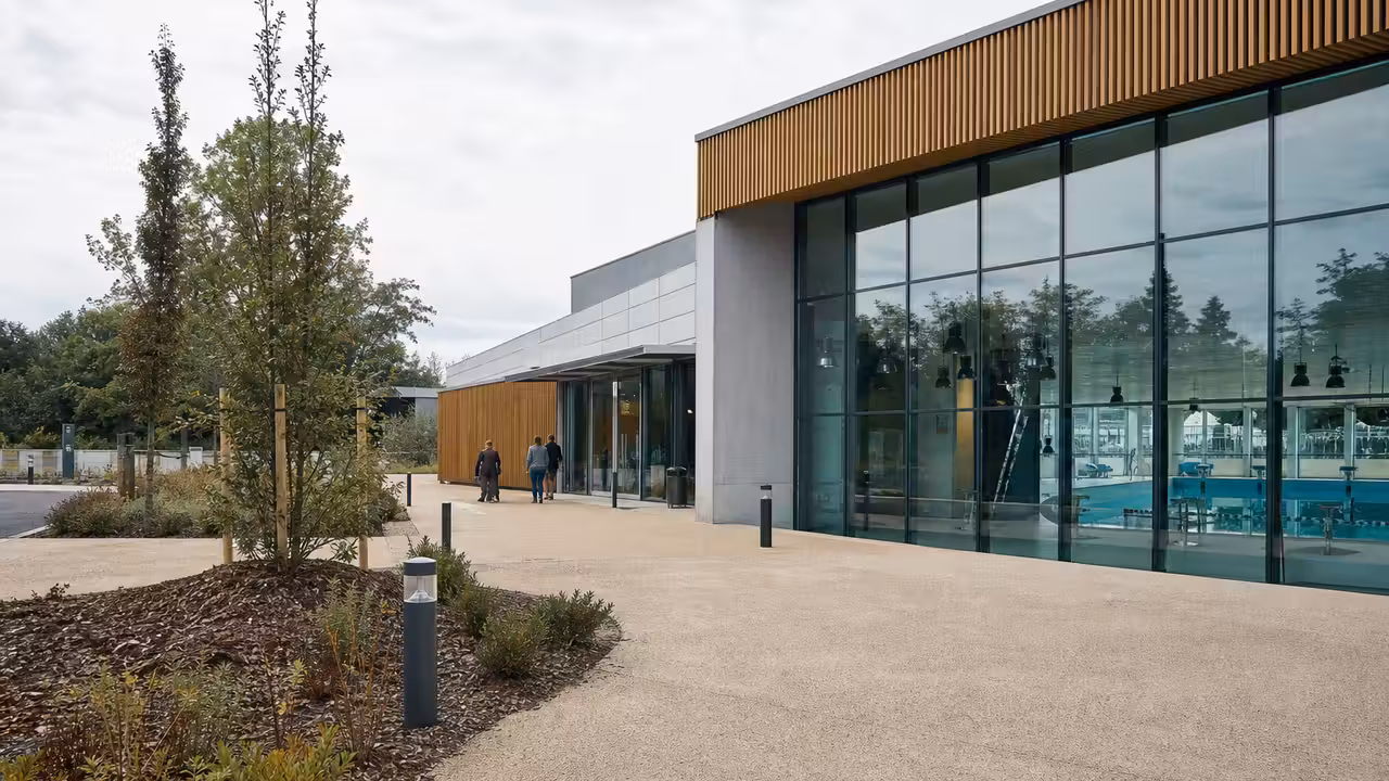 Vue extérieure d’un centre aquatique contemporain avec bassin intérieur visible à travers une façade vitrée