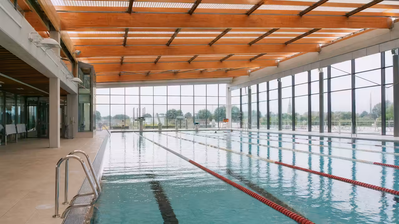 Bassin intérieur de 25 mètres dans un centre aquatique moderne, avec lignes d’eau et baies vitrées