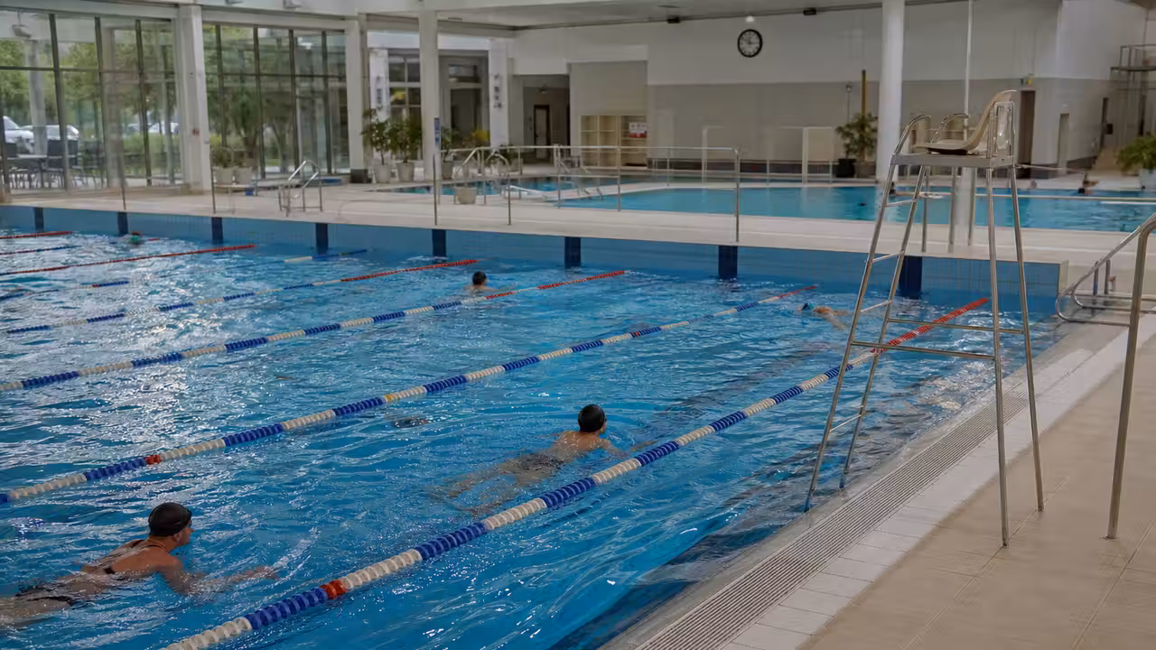 Nageurs dans les lignes d’eau d’une piscine municipale lumineuse, vus depuis le bord du bassin