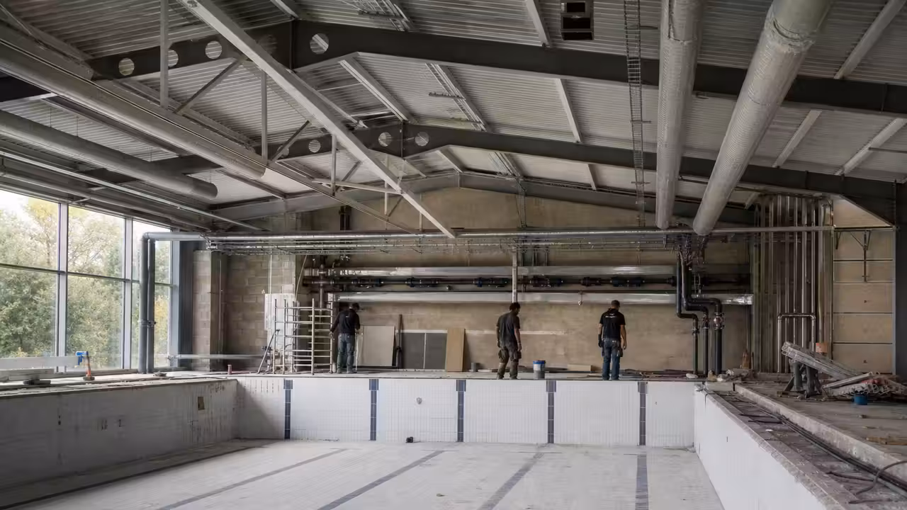 Bassin intérieur vide en rénovation, avec réseaux techniques apparents et charpente métallique restaurée