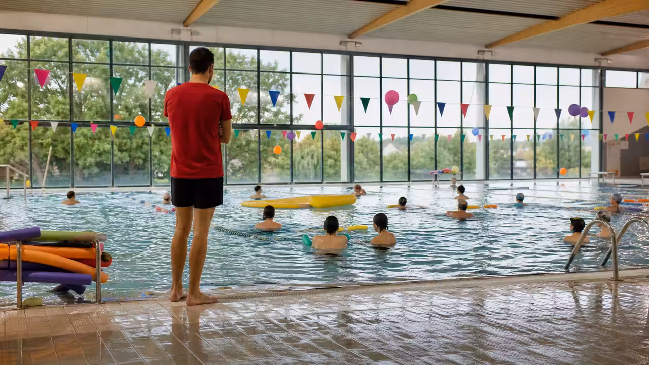 Animation aquatique dans un bassin municipal avec lignes d’eau, éclairage naturel et public en arrière-plan