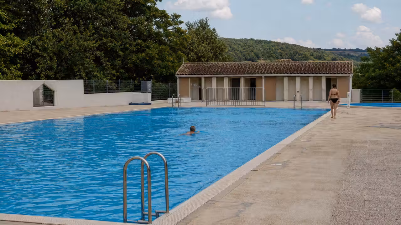 Bassin extérieur d’un équipement aquatique communal, entouré de plages minérales et d’un paysage végétal