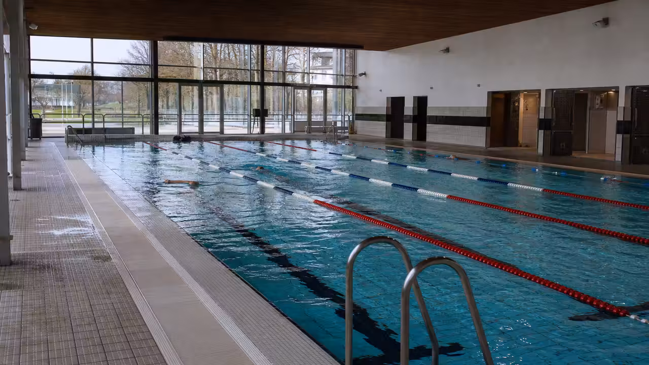 Bassin intérieur d’une piscine municipale moderne, avec couloirs de nage et vestiaires visibles en arrière-plan