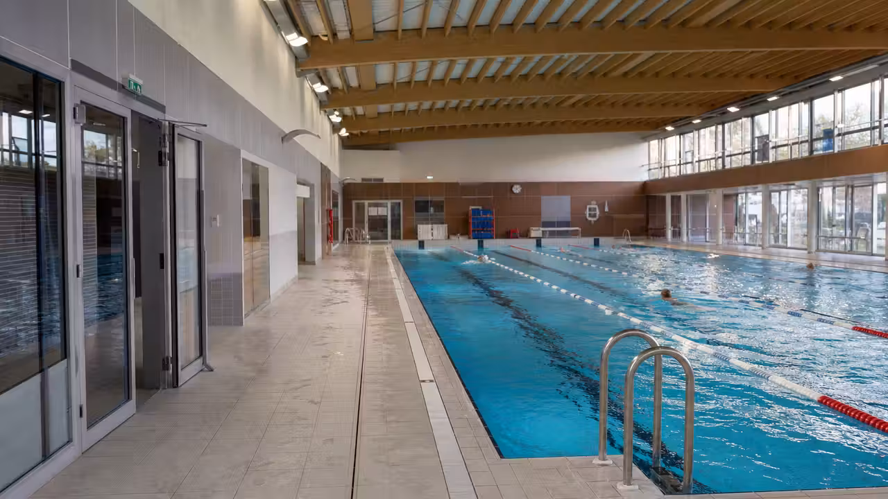 Bassin intérieur de piscine publique rénové, lignes d’eau calmes et vestiaires lumineux à l’arrière-plan
