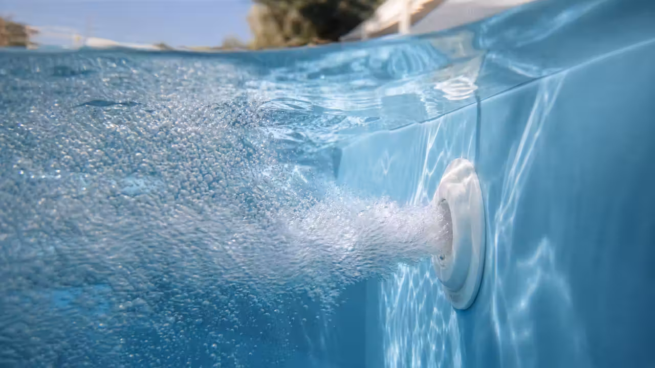 Buse de refoulement blanche projetant un jet chargé de fines bulles d'air sous la surface d'une piscine au liner bleu