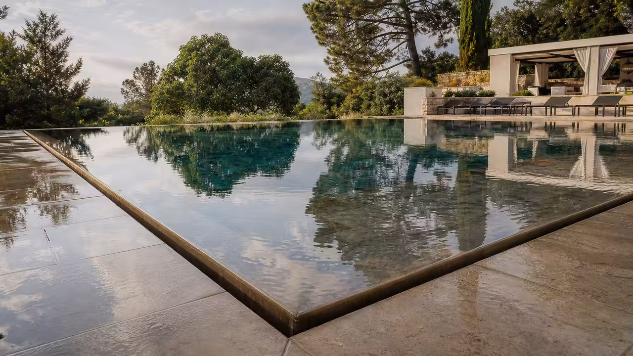 Piscine miroir contemporaine à débordement total, au niveau d’une terrasse minérale et d’un jardin planté