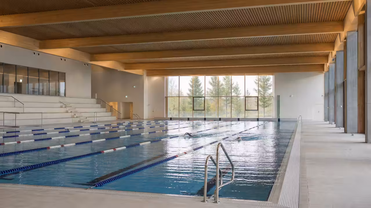 Bassin intérieur lumineux d’un centre aquatique moderne avec lignes de nage et baigneurs vus de dos