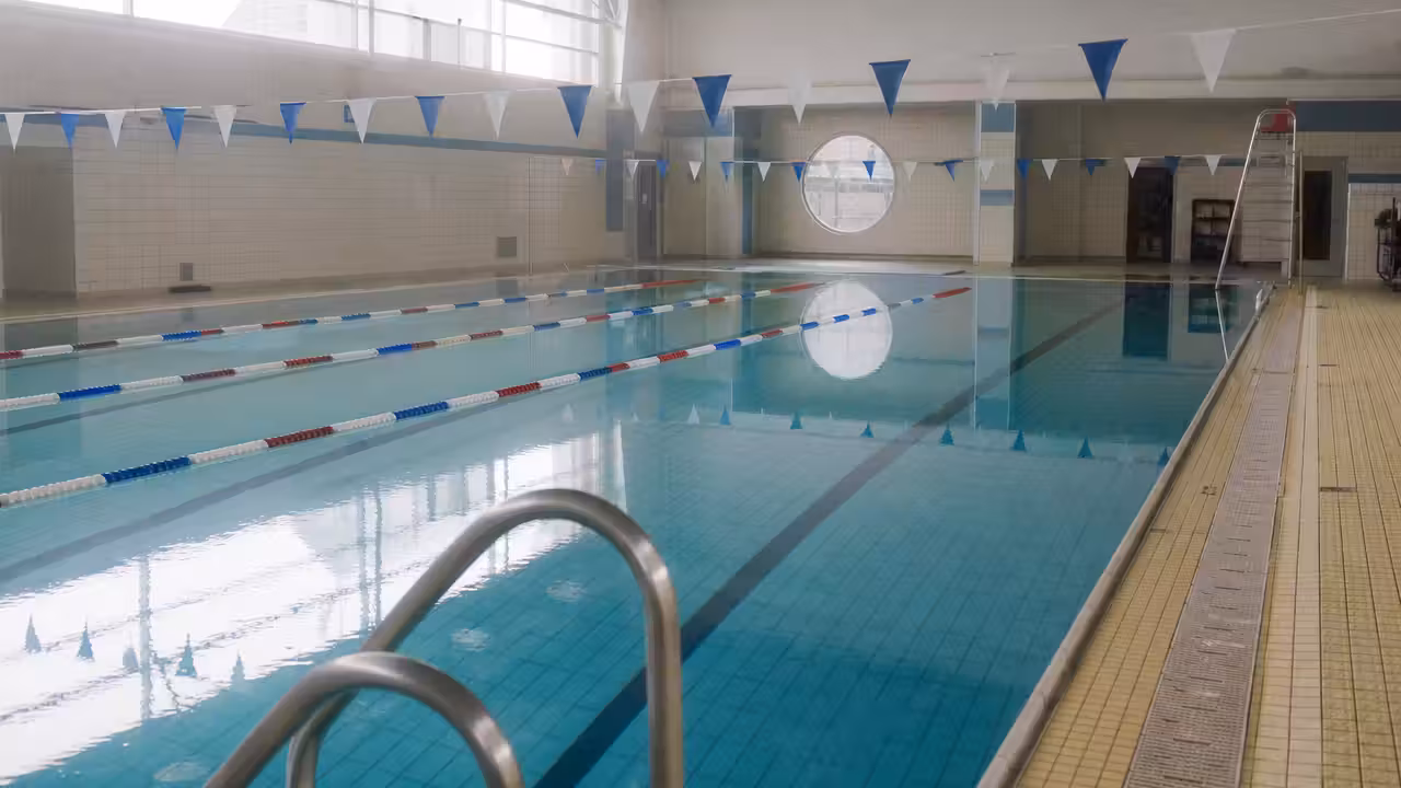 Bassin intérieur vide d’une piscine municipale, avec lignes d’eau et équipements techniques en arrière-plan