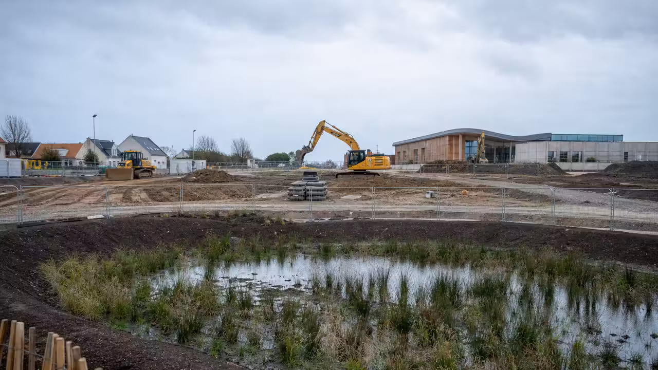 Terrain préparé pour un centre aquatique avec engins de chantier et noues paysagères sous un ciel du Nord