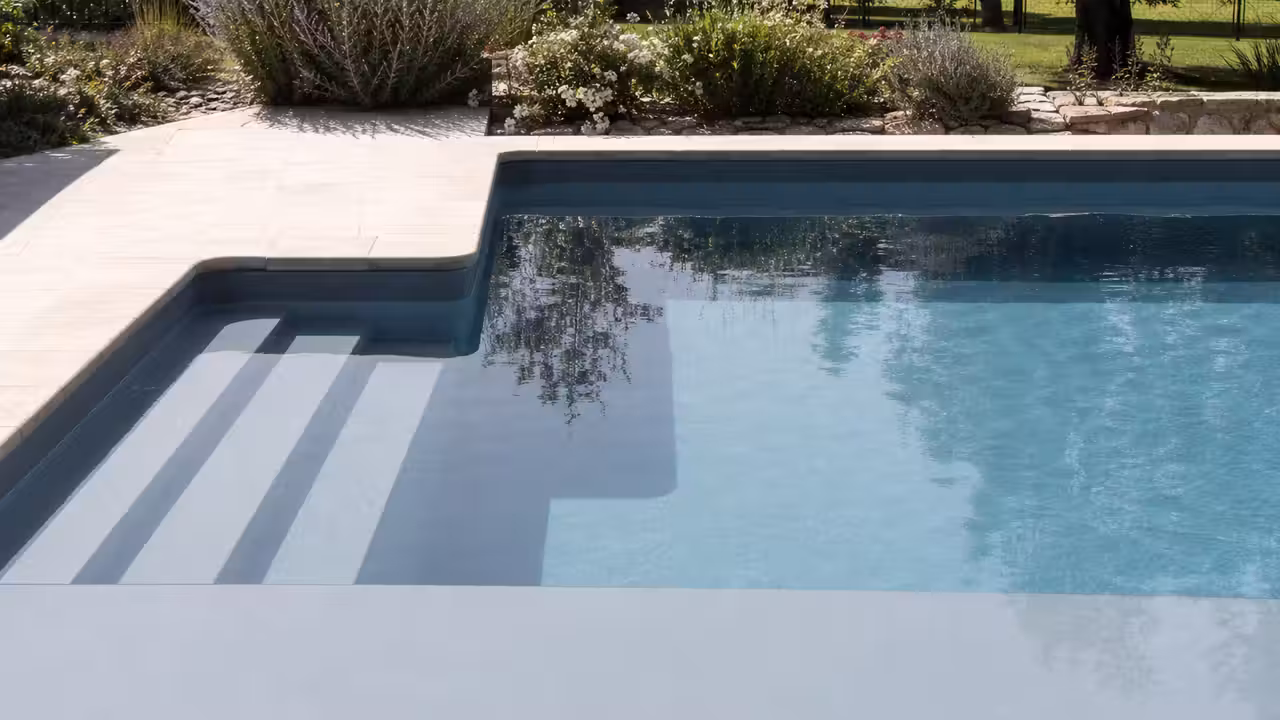 Gros plan d’un liner gris bleu parfaitement tendu dans un bassin avec escalier immergé et margelles claires